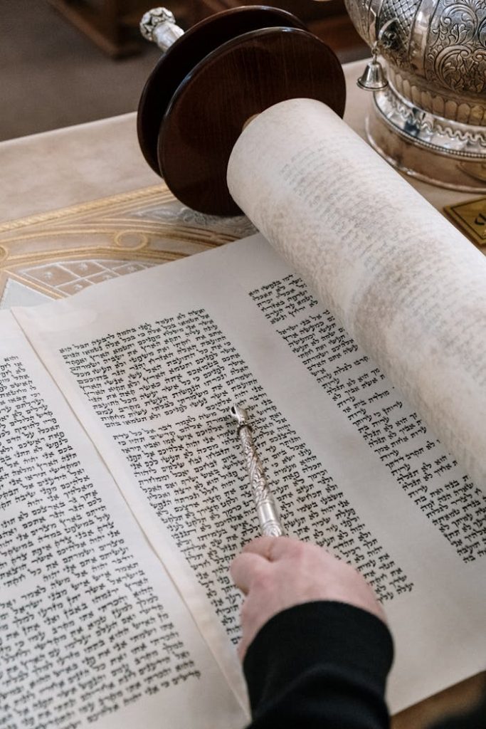 A detailed close-up of a Torah scroll with a yad pointer being used during a religious ceremony.