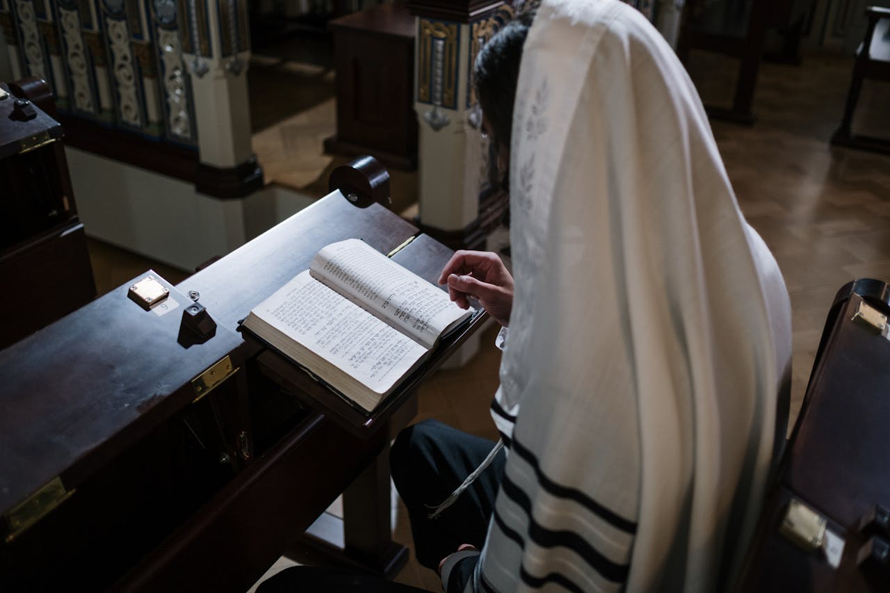 A person wearing a tallit reads from a Torah inside a synagogue, emphasizing religious devotion.